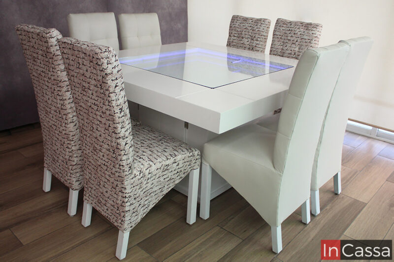En esta foto vemos el comedor blanco con sus 8 sillas tapizadas. Su mesa destaca gracias a su arenero central, el cual se muestra completamente descubierto con su sistema de iluminación LED encendido en una tonalidad purpura.
