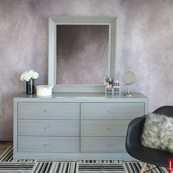 Tocador contemporáneo en acabado gris cenizo claro, el mueble consta de un tocador de 6 cajones y un espejo rectangular, todo instalado en una pared gris.