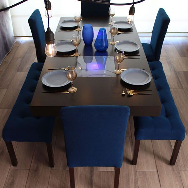Moderno comedor para 8 personas conformado por una mesa color chocolate con dos centros de mesa iluminados, además de 4 sillas y 2 bancas tapizadas en lino pavorreal. El comedor se presenta decorado con algunos jarrones y vajillas.