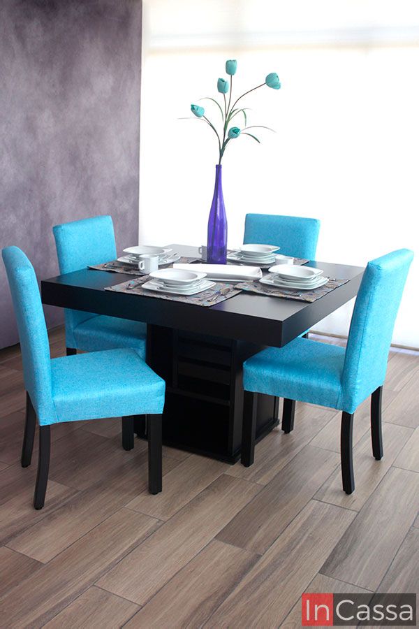 Comedor para 4 personas de mesa color chocolate completa y cuatro sillas tapizadas en tela pliana color aqua. El mueble está instalado en una habitación con piso de madera y pared gris iluminada gracias a una venta completa.