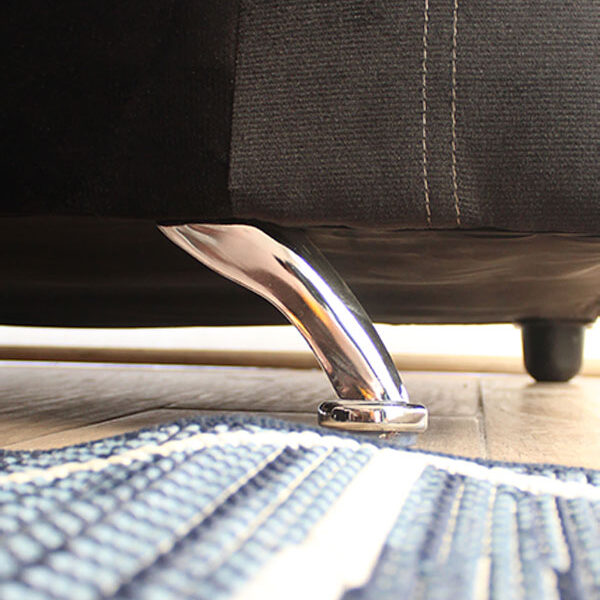 La imagen enfoca las patas que sostienen cada love seat tapizado en suede negro, en la cuál se puede apreciar que las patas delanteras son metálicas y tienen un acabado cromado, mientras que las traseras son más pequeñas de plástico en color café.