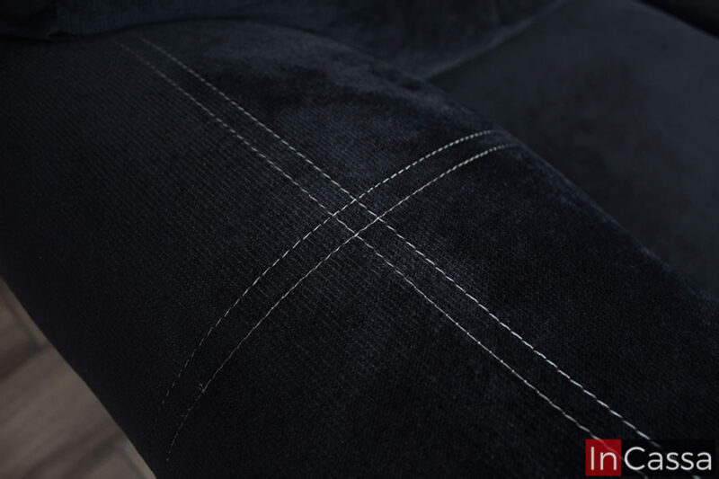 La imagen enfoca las finas costuras blancas en la tela suede negro de los descansa brazos, así como un mejor vistazo a la textura de la misma, que igualmente puede apreciarse en el resto del love seat.