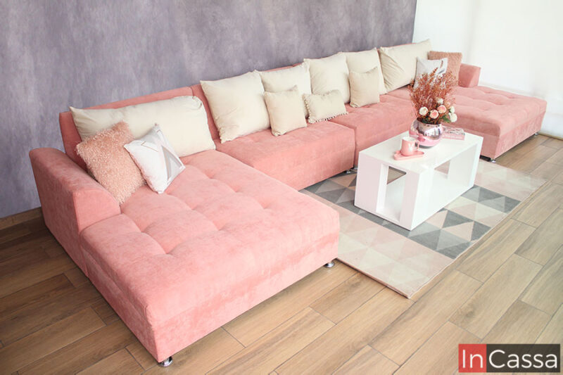 Sala Jumbo en U tapizada en suede color rosa con 6 cojines grandes color hueso igualmente tapizados en tela suede.