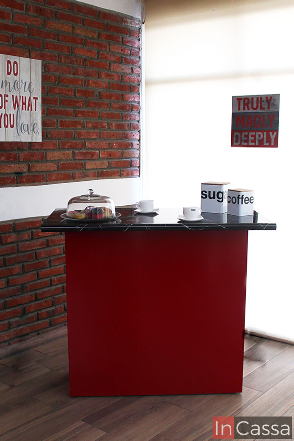 Moderna barra para cocina roja con cubierta de formica estilo mármol negro, el mueble es presentado en una estancia con pared de ladrillo, ventana completa y piso de madera.
