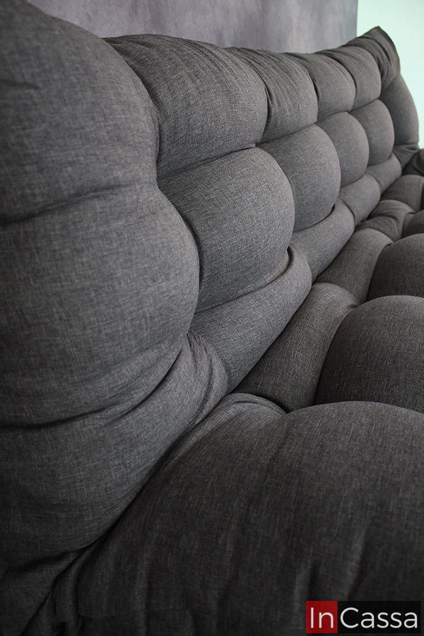 La imagen destaca el acabado capitoneado presente en el asiento así como en el respaldo del sofá cama, además de la textura de la tela lino mouse utilizada en el tapizado de todo el mueble.