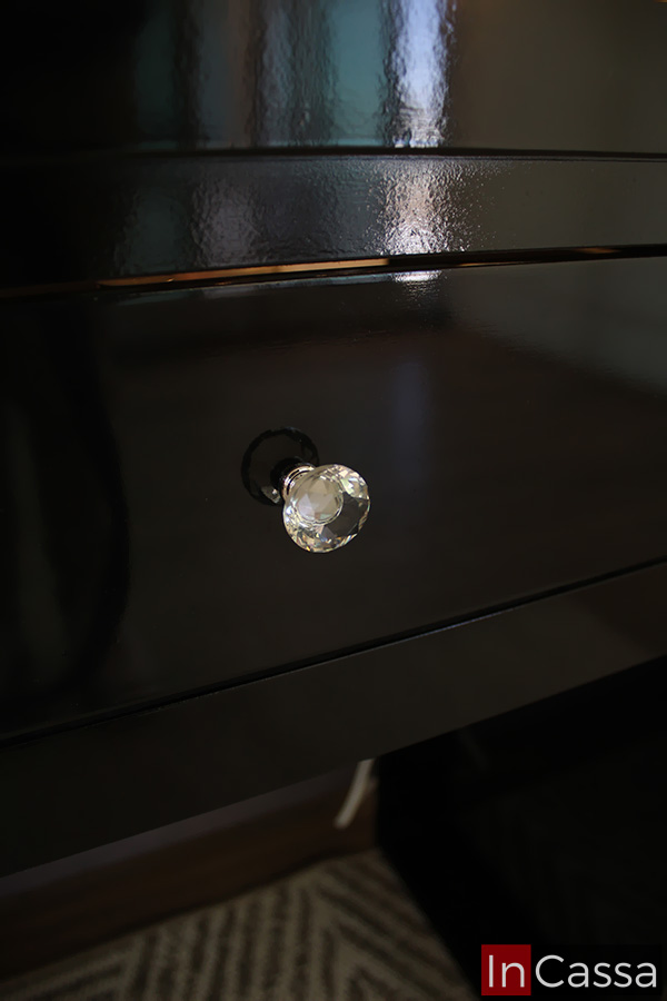 La toma se enfoca en la jaladera de estilo diamante integrada al cajón; por la cercanía de la foto, también queda resaltado el acabado brillante de la pintura negra del tocador.