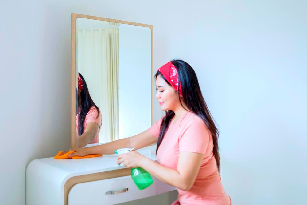 La imagen muestra a una mujer realizando la limpieza de un tocador con espejo.