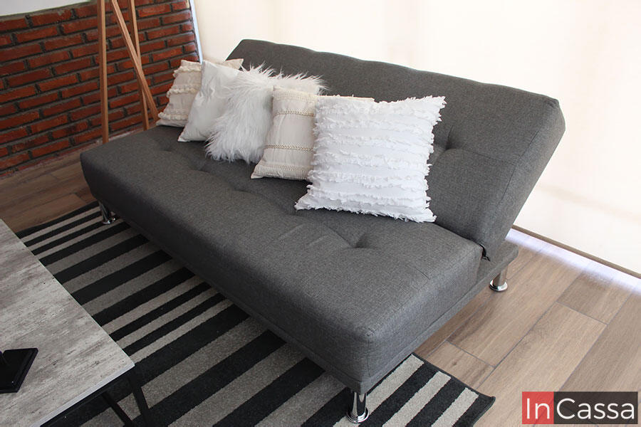 Moderno sofá cama tapizado en tela lino mouse decorado con cojines blancos de diferentes estilos, el sofá cuenta con un mecanismo que le permite bajar el respaldo para convertirlo en una cama individual.