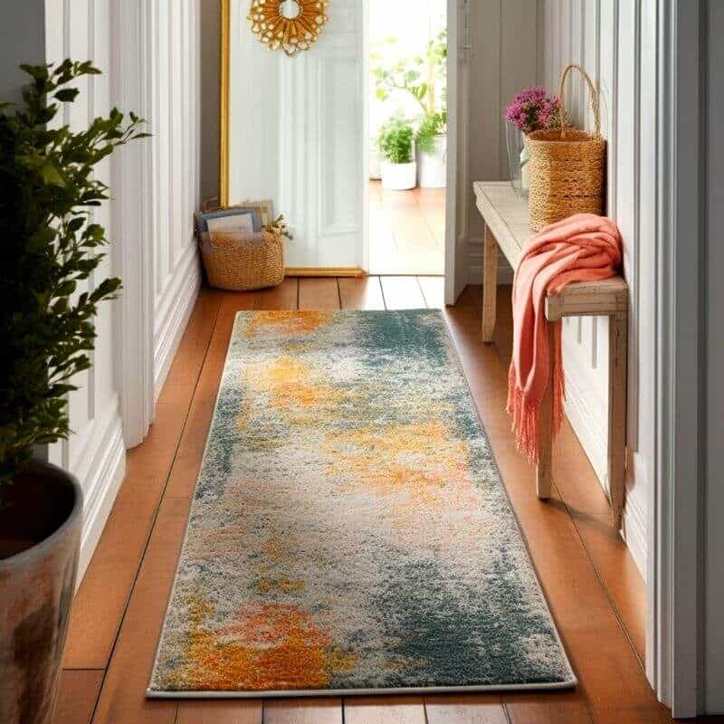 Recibidor con alfombra colorida en pasillo luminoso, junto a una banca y decoraciones acogedoras.