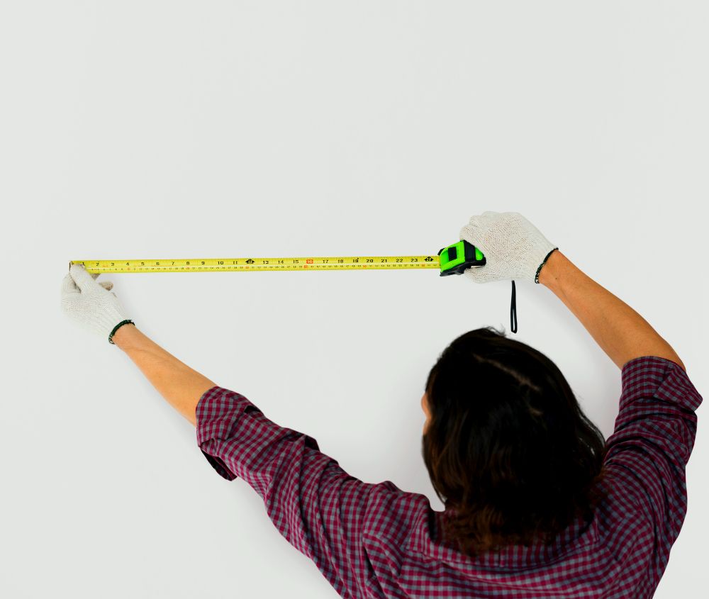 La imagen muestra a una persona midiendo parte de una pared con una cinta metrica.