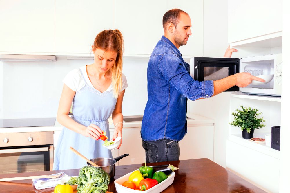 La foto muestra a una pareja preparando sus alimentos haciendo uso del equipamiento de su cocina.