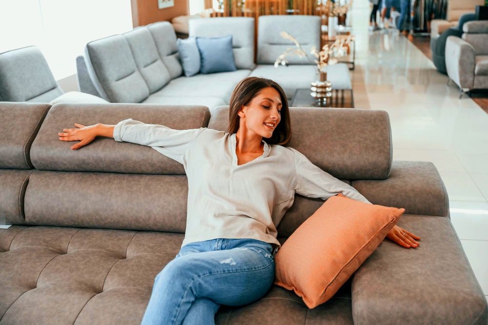 La foto muestra a una mujer probando la comodidad de distintos sofás de diferentes estilos y colores.