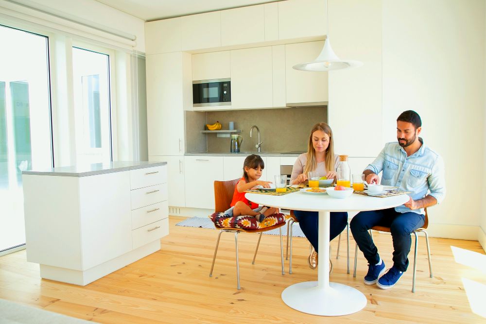 La imagen muestra a una familia tomando su desayuno en una mesa circular instalada cerca de su cocina, economizando espacio y teniendo una distribución más práctica de los muebles.