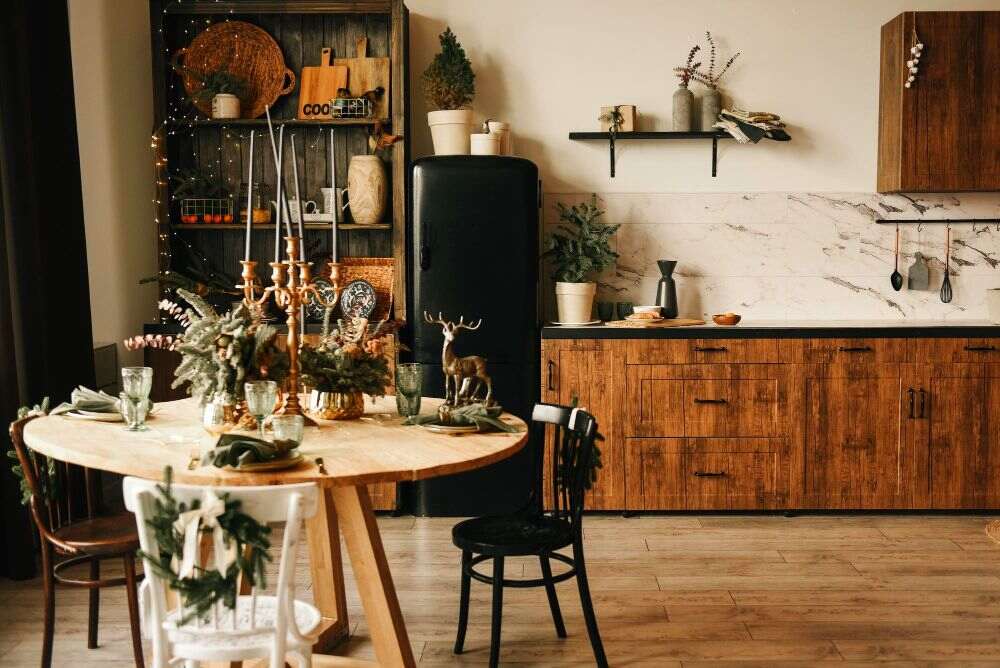 Imagen de una cocina rústica fabricada de madera natural acompañada de un pequeño comedor circular y un estante rústico ambos muebles de madera natural igualmente.