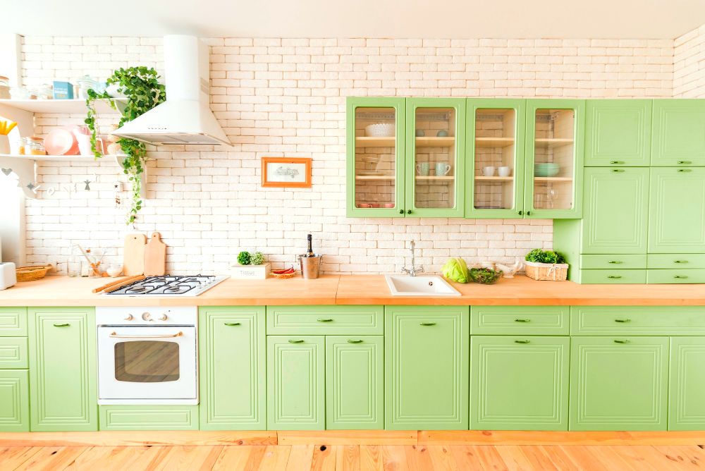 Una cocina lineal de estilo vintage en color verde limón con cubierta de madera natural, la cuál cuenta con una gran cantidad de compartimentos además de algunos estantes de pared.
