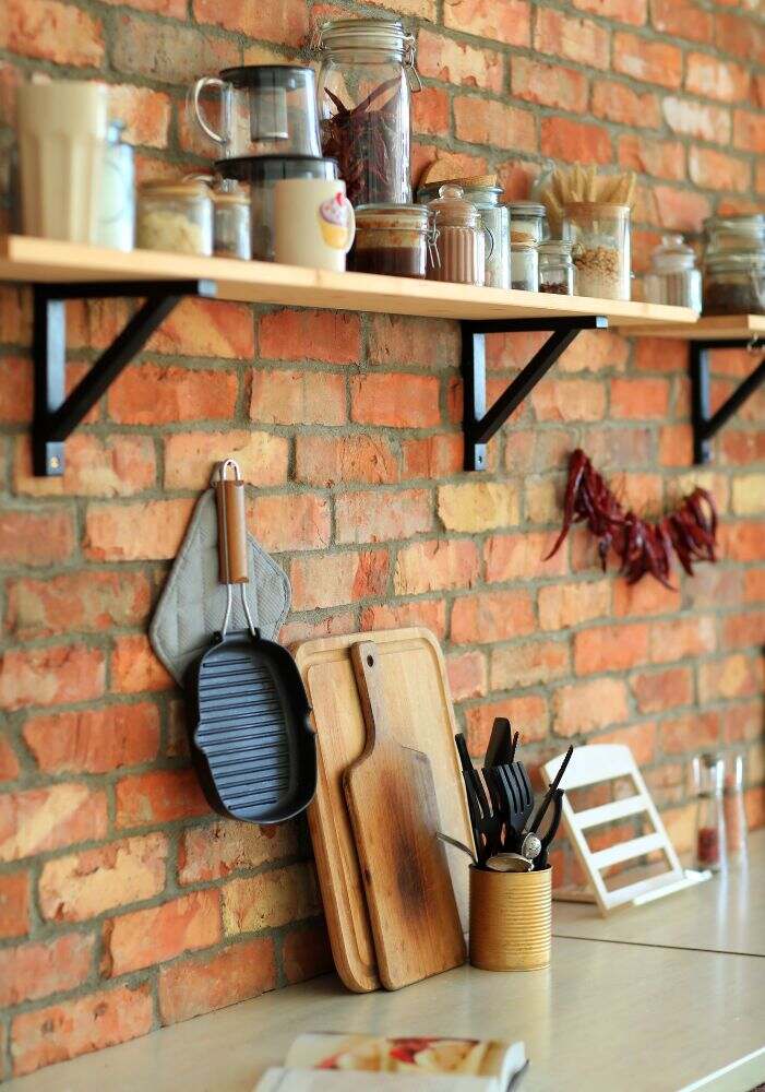 Una gran juego de utensilios y frascos con especias distribuidos en estantes y soportes de pared, lo cuál da una cálida decoración que además provee mayor funcionalidad a una cocina.