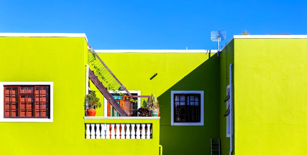 La parte superior de una casa en color verde claro con algunos detalles en blanco y ventanas con marco de madera en tono maple.