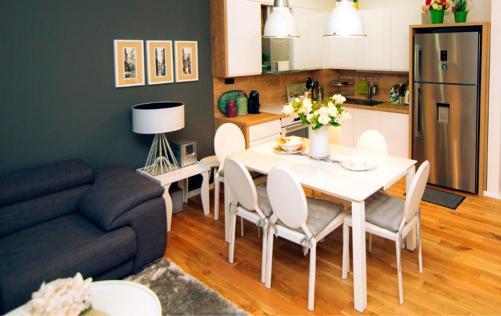 Foto de la estancia de un apartamento en la cuál puede verse un espacio abierto con una sala, cocina en escuadra y un comedor minimalista para 6 personas.