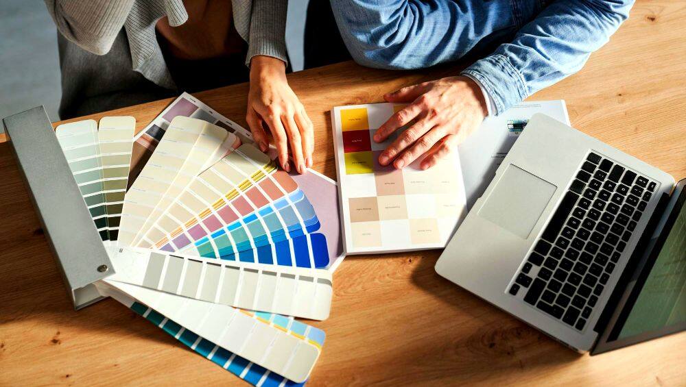 La foto muestra a una pareja haciendo uso de una gran colección de paletas de colores en diferentes tonos para escoger el que mejor se adecue en su hogar.