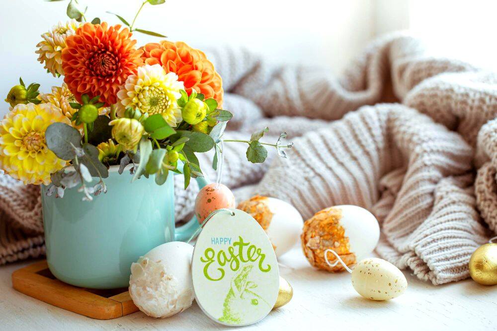 Una imagen que presenta una cobija tejida y una taza con flores acompañada por una gran variedad de huevos de Pascua; un conjunto excelente para la decoración de  cualquier hogar en temporadas de Pascua.