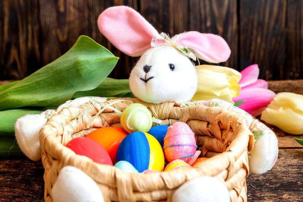Una bonita canasta decorada con un icónico conejo de Pascua de peluche así como varios huevos de diferentes colores.