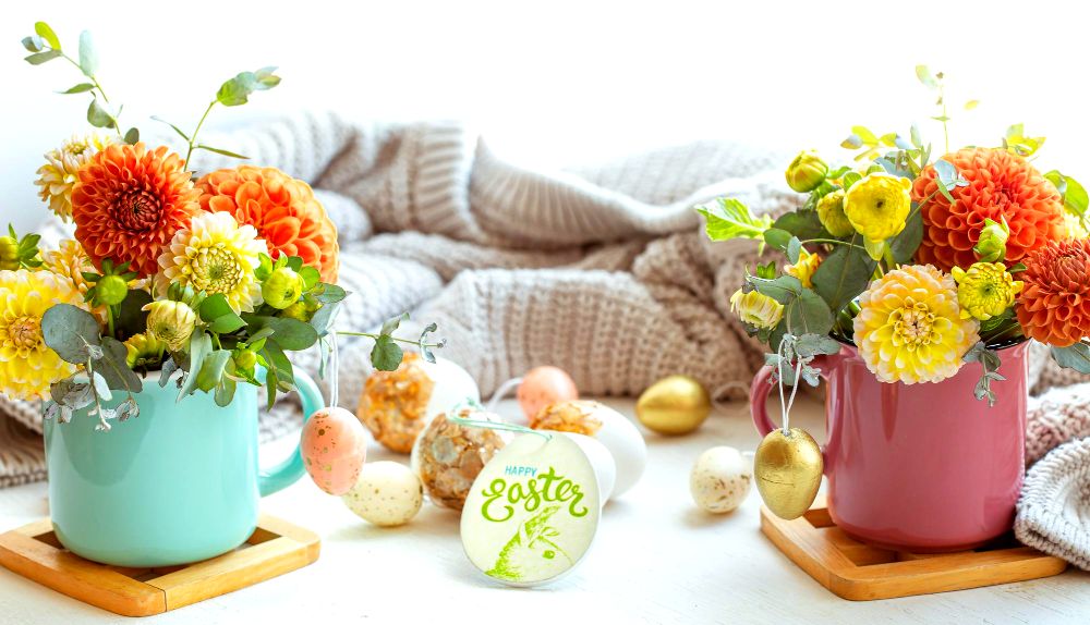 Una foto en la que se muestra una colección de decoraciones tradicionales para Pascua, entre las que resaltan las flores de colores cálidos y bonitos huevos de Pascua, todos acompañados por algunos detalles de madera natural y tejidos de colores neutros.
