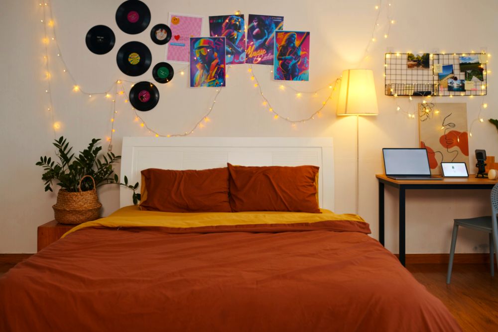 Una foto frontal de una recámara de estilo aesthetic bastante moderno, en la que vemos una cama minimalista junto a un escritorio de estilo industrial. El lugar se encuentra decorado por una colección de vinilos, posters, plantas decorativas y una gran var