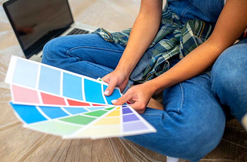 La imagen muestra a una persona haciendo uso de una colección de muestrarios de colores, escogiendo el adecuado para su habitación.
