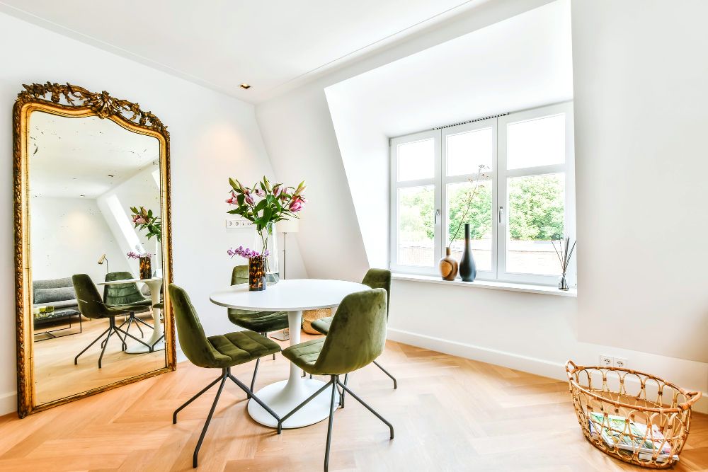 Foto de un comedor minimalista con mesa circular para 4 personas, instalado junto a un gran espejo con un elegante marco dorado, cuyo reflejo permite apreciar el resto de la estancia.