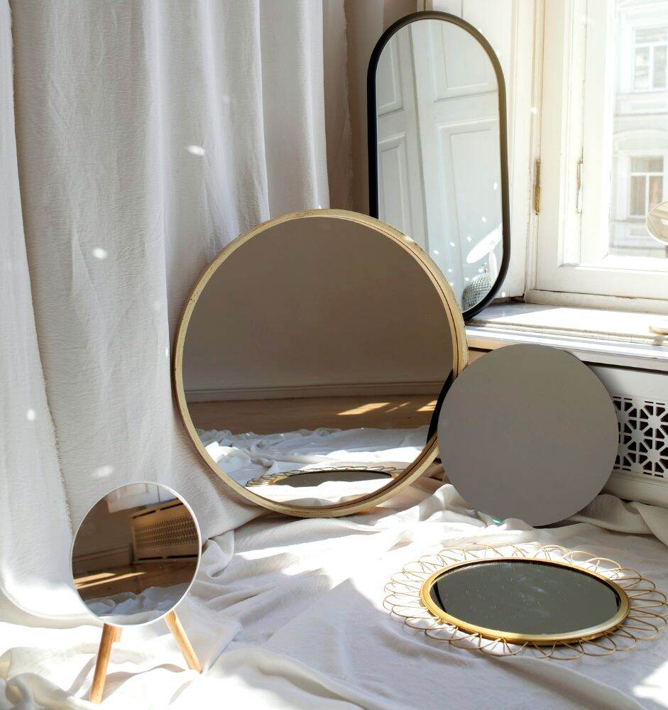 La imagen muestra una colección de espejos decorativos, entre los que se pueden apreciar dos espejos con marco dorado circular, un espejo circular más pequeño para tocador y un espejo de marco negro ovalado.