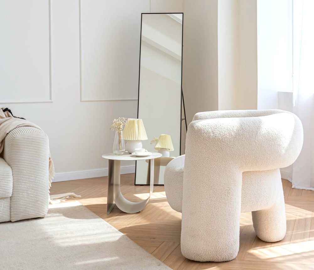 La foto muestra una sala blanca con un atractivo diseño muy moderno, la cuál esta acompañada por una pequeña mesa de auxiliar y un espejo rectangular de cuerpo completo minimalista.