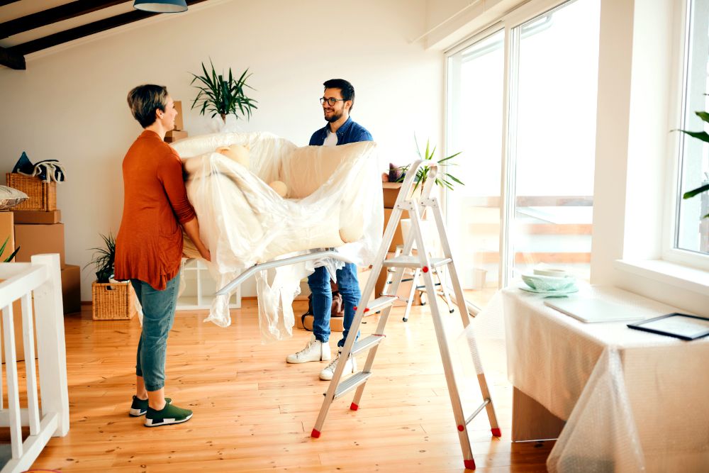 La imagen muestra a una pareja instalando un sillón en el salón de su nuevo hogar.