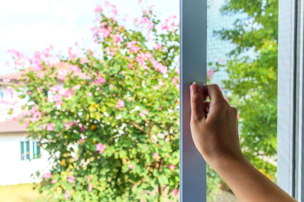 La imagen muestra a una persona abriendo las ventanas de su casa para tener una mejor ventilación.
