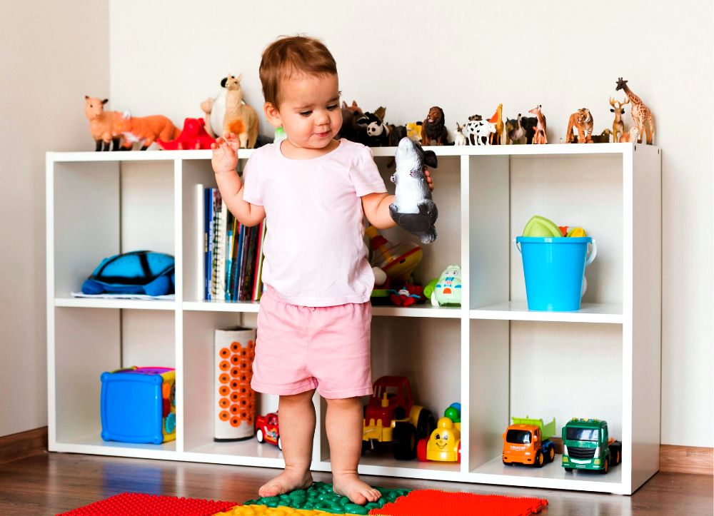 La fotografía muestra a un pequeño jugando con uno de sus muchos juguetes de animales, los cuales se encuentran muy bien guardados en un mueble juguetero con múltiples estantes.