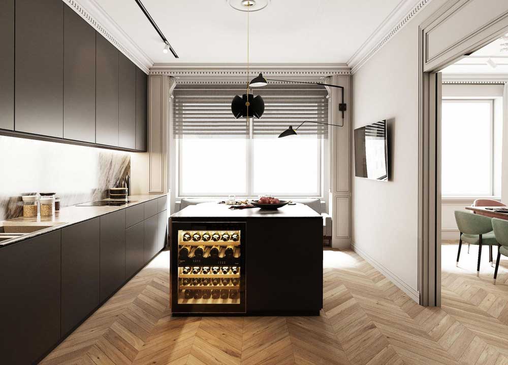 Una vista frontal resalta la sofisticada isla central en acabado negro mate, equipada con una cava iluminada para botellas de vino, perfectamente integrada al diseño. El espacio se enmarca con un elegante piso en espiga, gabinetes sin tiradores en tono oscuro y detalles arquitectónicos clásicos que combinan lo moderno con lo atemporal. Al fondo, se aprecia la luz natural filtrada por persianas y un comedor adyacente con sillas verdes que añaden un toque de color.