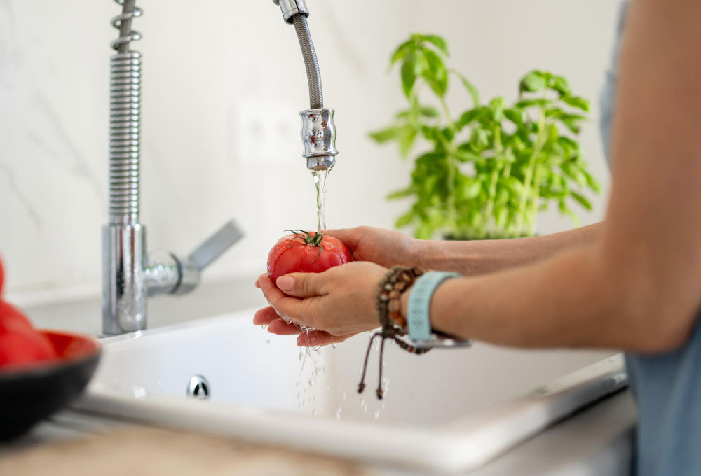 Mulher lavando tomate fresco na pia da cozinha
