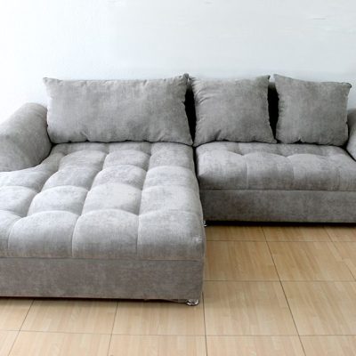 La Sala Esquinera modelo BANGLADÉS se muestra en una toma frontal completa, resaltando su tapizado en suede gris perla. Los asientos capitonados y cojines sueltos brindan gran comodidad, mientras que sus brazos rectos y patas metálicas aportan un estilo moderno y elegante.