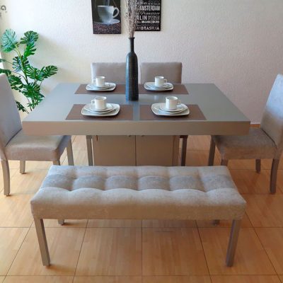 Una toma desde arriba muestra el comedor Cambridge para 6 personas completo, con mesa central cuadrada en color silver, banca tapizada capitonada y cuatro sillas en tono gris perla. El diseño moderno armoniza con la decoración neutra del espacio.