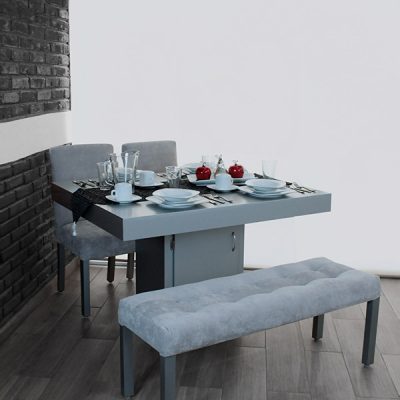 La imagen muestra el comedor Cambridge para 4 personas en tono silver, con mesa de base central tipo gabinete, sillas tapizadas en tacto suave y una banca con acabado capitonado. Ideal para espacios modernos y elegantes.