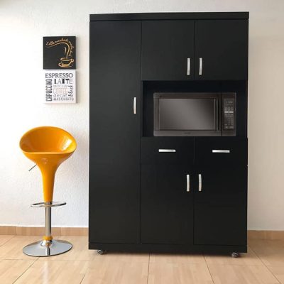 La imagen muestra la elegante Alacena para Microondas MÁLAGA en acabado chocolate mate, visto de frente y en plano completo. Destaca su diseño funcional con múltiples compartimentos y espacio central para microondas, adornado con jaladeras metálicas plateadas. A la izquierda, un banco alto amarillo crea un contraste vibrante.