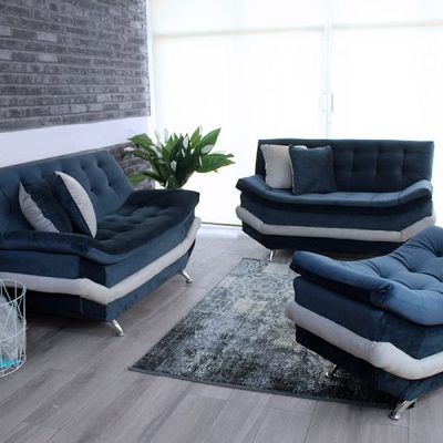 La imagen muestra la Sala Modelo Murcia en un elegante tapizado de suede azul marino, compuesta por dos love seat y un taburete. Su diseño moderno de líneas suaves y costuras capitonadas resalta sobre un ambiente contemporáneo con muros de ladrillo gris y piso tipo madera, creando una atmósfera acogedora y sofisticada ideal para cualquier estancia.