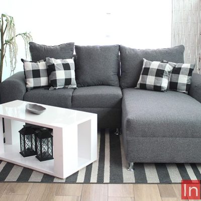 Sala minimalista en escuadra tapizada en lino mouse, decorada con 4 cojines pequeños y acompañada de una mesa de centro blanca. La sala es presentada en una estancia con piso de madera y una venta de pantalla completa.