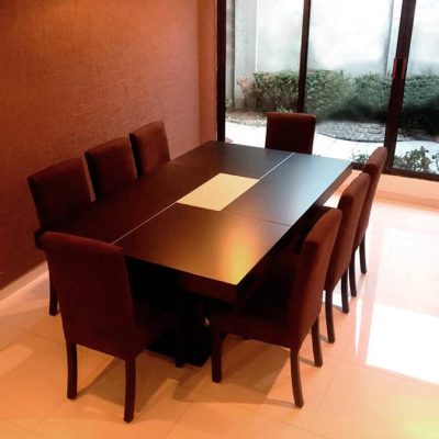 La imagen muestra el Comedor Modelo RABAT para 8 personas, con mesa en tono chocolate y sillas tapizadas en suede color chocolate. Su diseño elegante y sobrio crea un ambiente cálido y moderno ideal para comedores amplios.